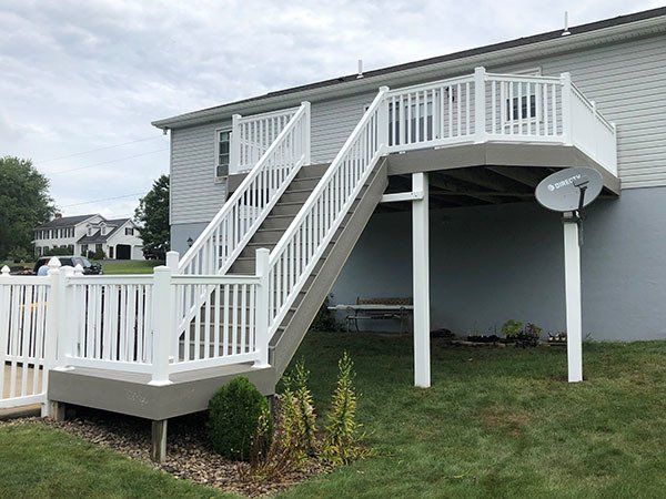 White-railed accessible ramp and stairs leading to a raised deck on a gray house with a satellite dish.