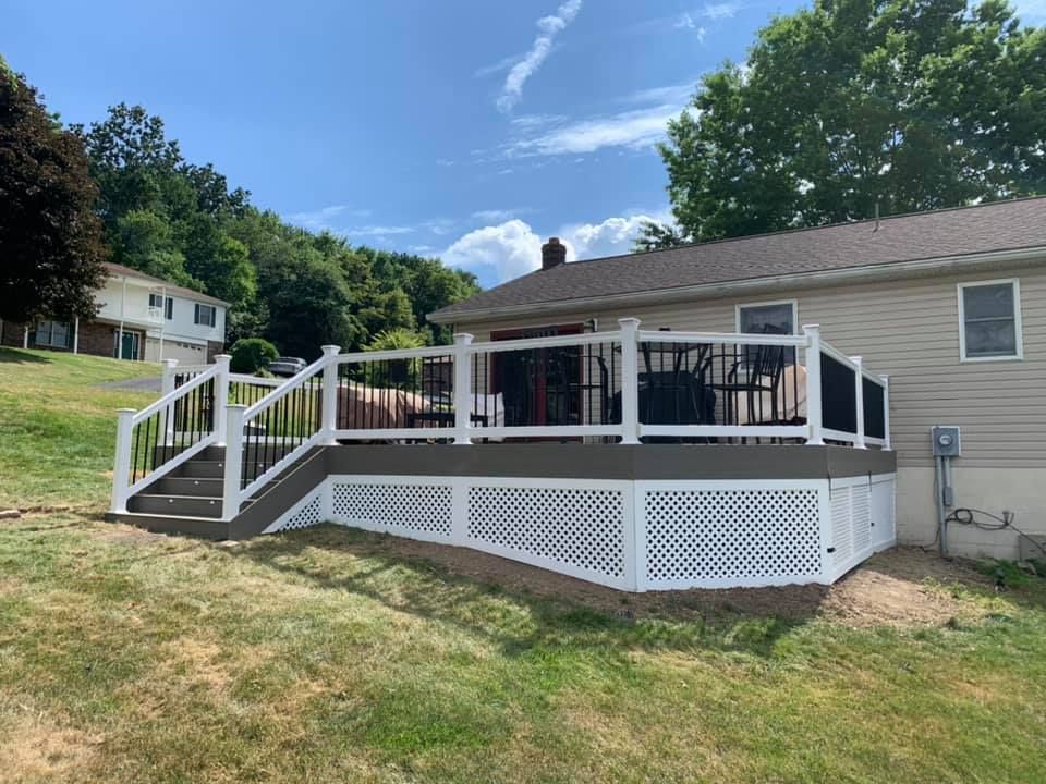Back deck with white railings and lattice skirting on a beige house, beside a grassy yard.