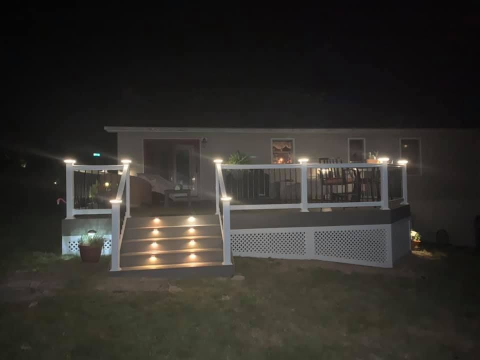 Nighttime view of a lit house porch with steps, white railings, and lattice skirting
