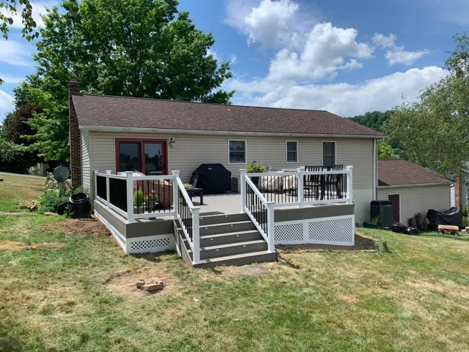 Small beige house with a front deck and stairs in a grassy yard under a blue sky