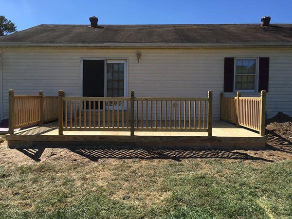Wooden deck with railings attached to a white house in a grassy yard