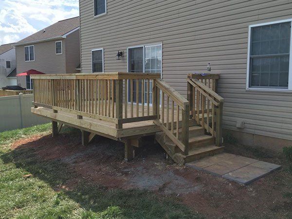 Wooden backyard deck with railing and steps beside a beige house