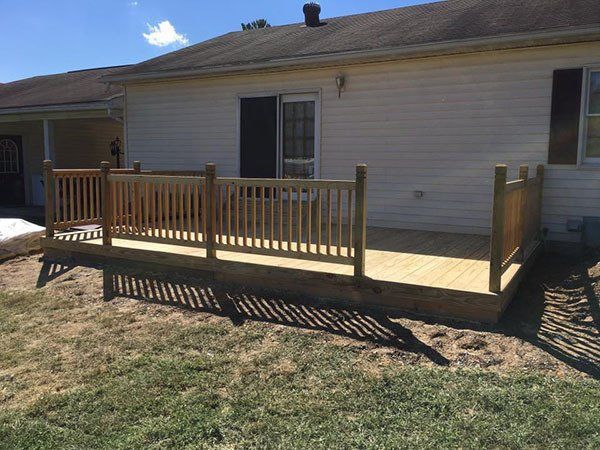 Backyard wooden deck attached to a beige house, with railings and steps over dry grass.
