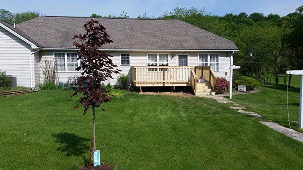 Single-story house with white siding, a wooden deck, and a large green lawn under a clear sky