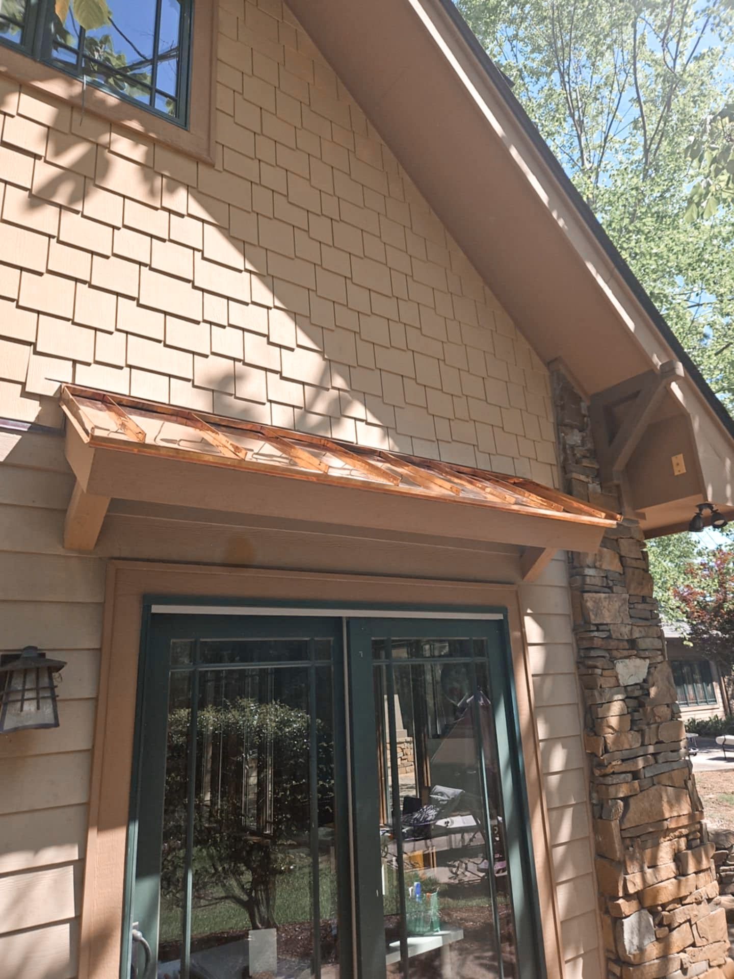 Tan shingled building with a small wooden awning over green doors. Stone pillar to the right.