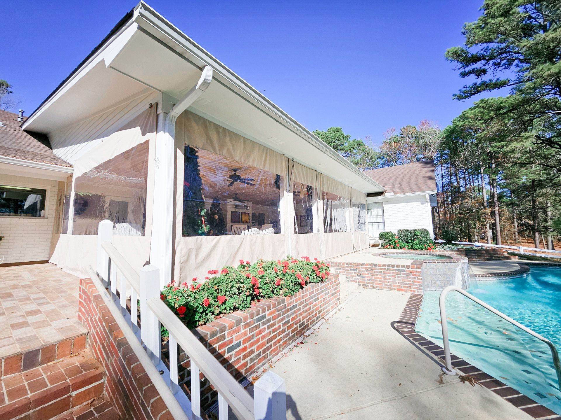 Exterior of a house with a screened patio next to a swimming pool. Red brick and white railing.