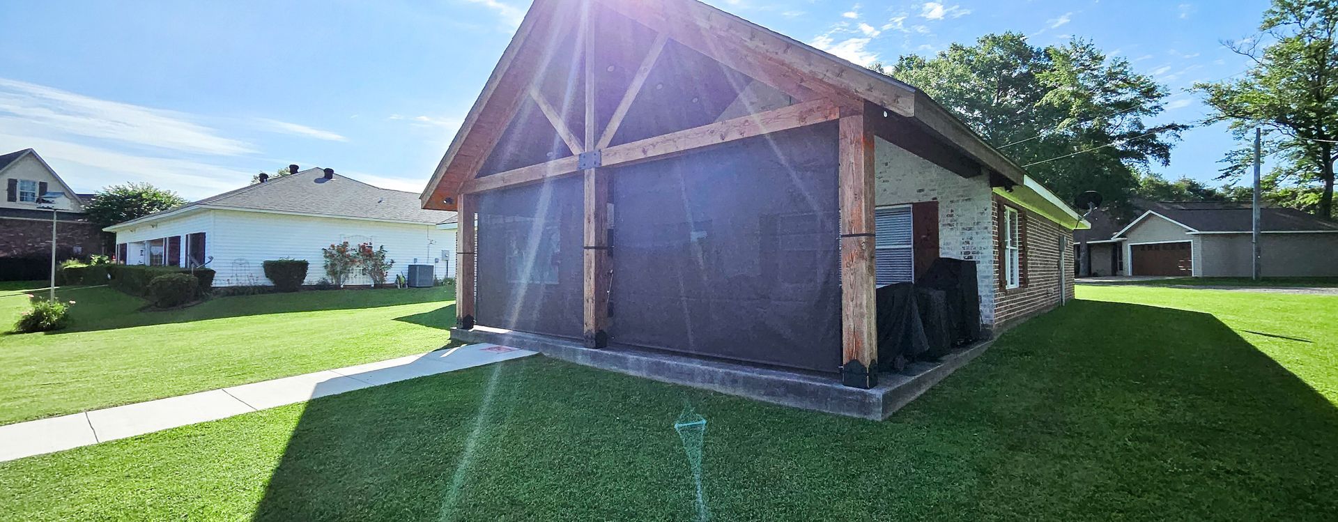 A light-colored building with brown accents and garage doors, lawn, and other houses on a sunny day.