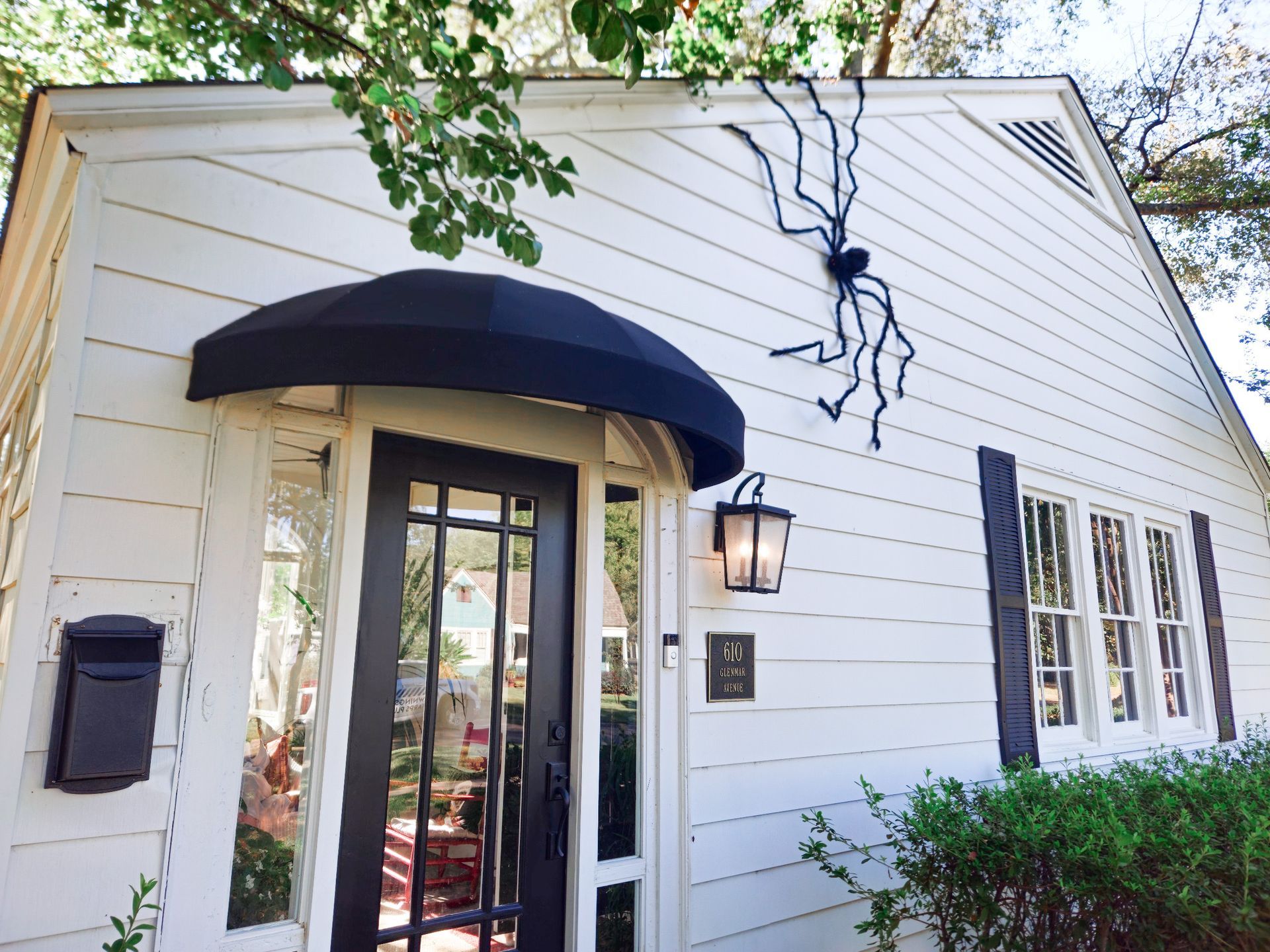 White house with black door, awning, shutters, and large spider decoration.