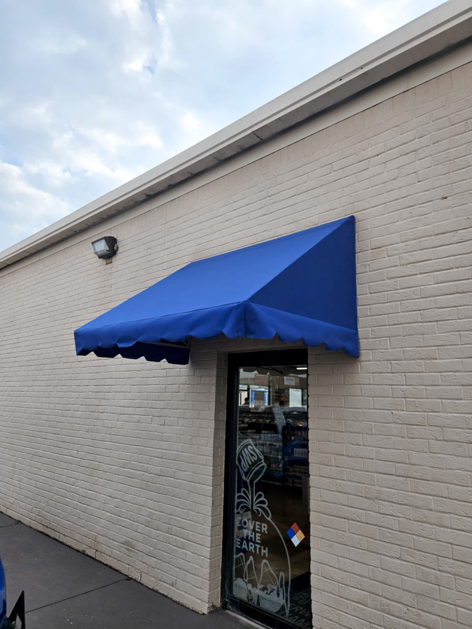 Blue awning over a glass door on a tan brick building.