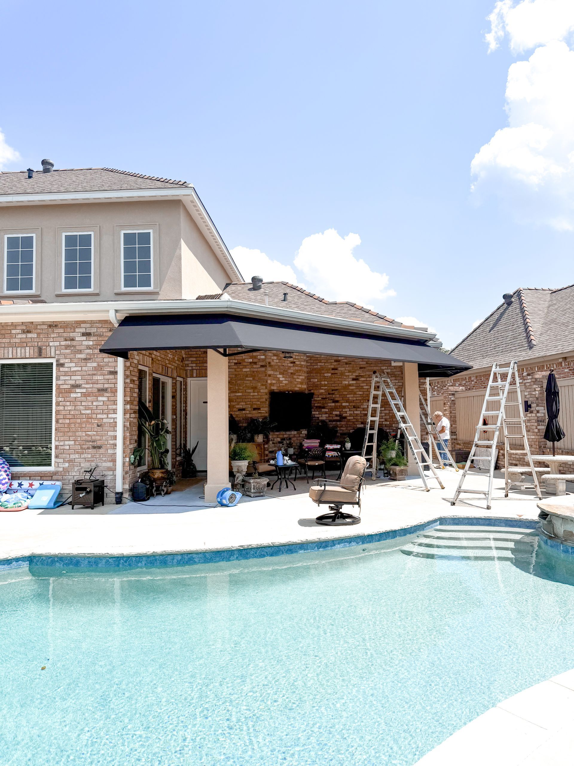 Poolside view of a home with an outdoor patio under construction with ladders, a pool, and blue sky.