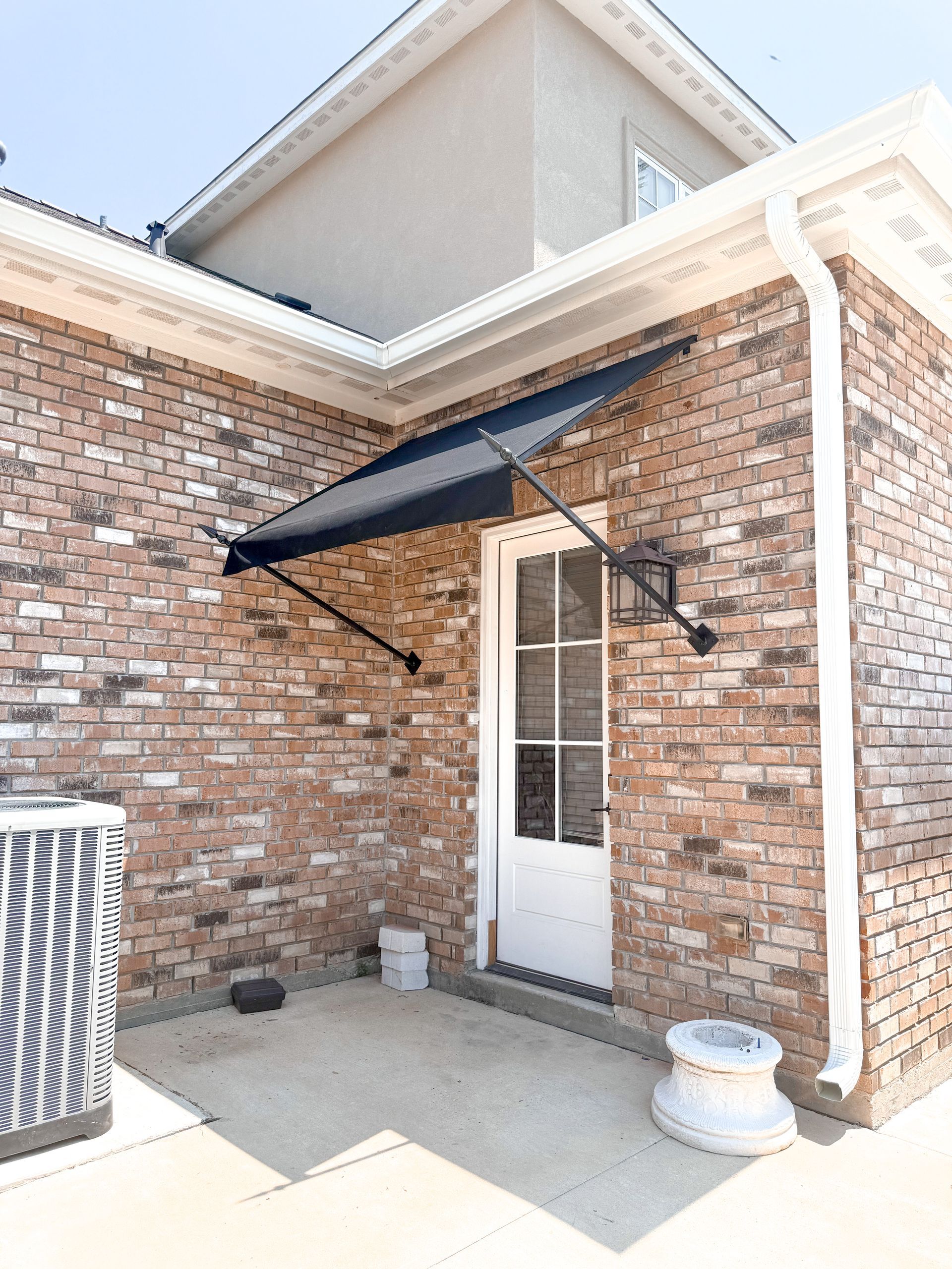 Black awning over a white door on a brick house, exterior view.