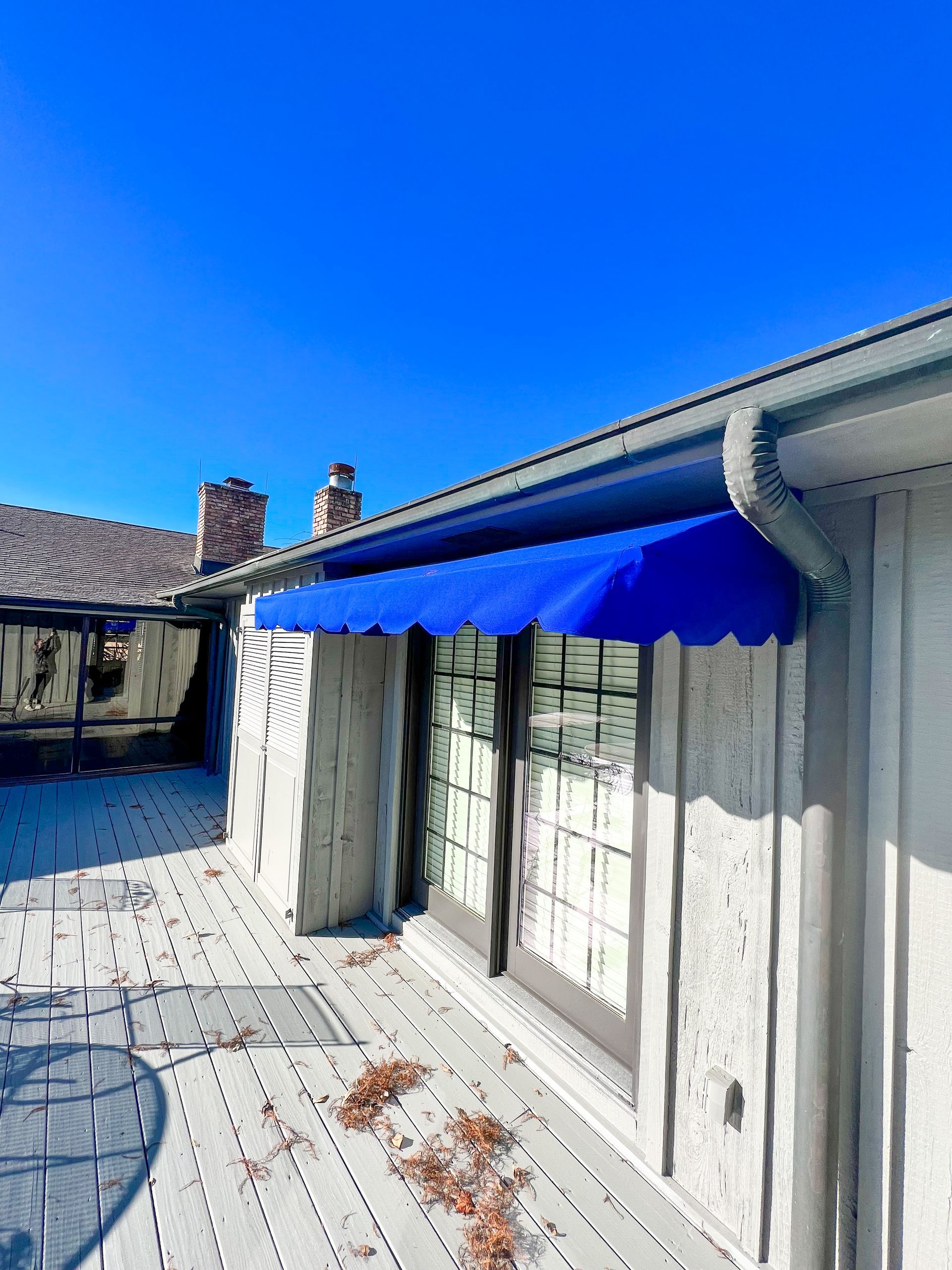 Blue awning over a window on a white house, with a blue sky.