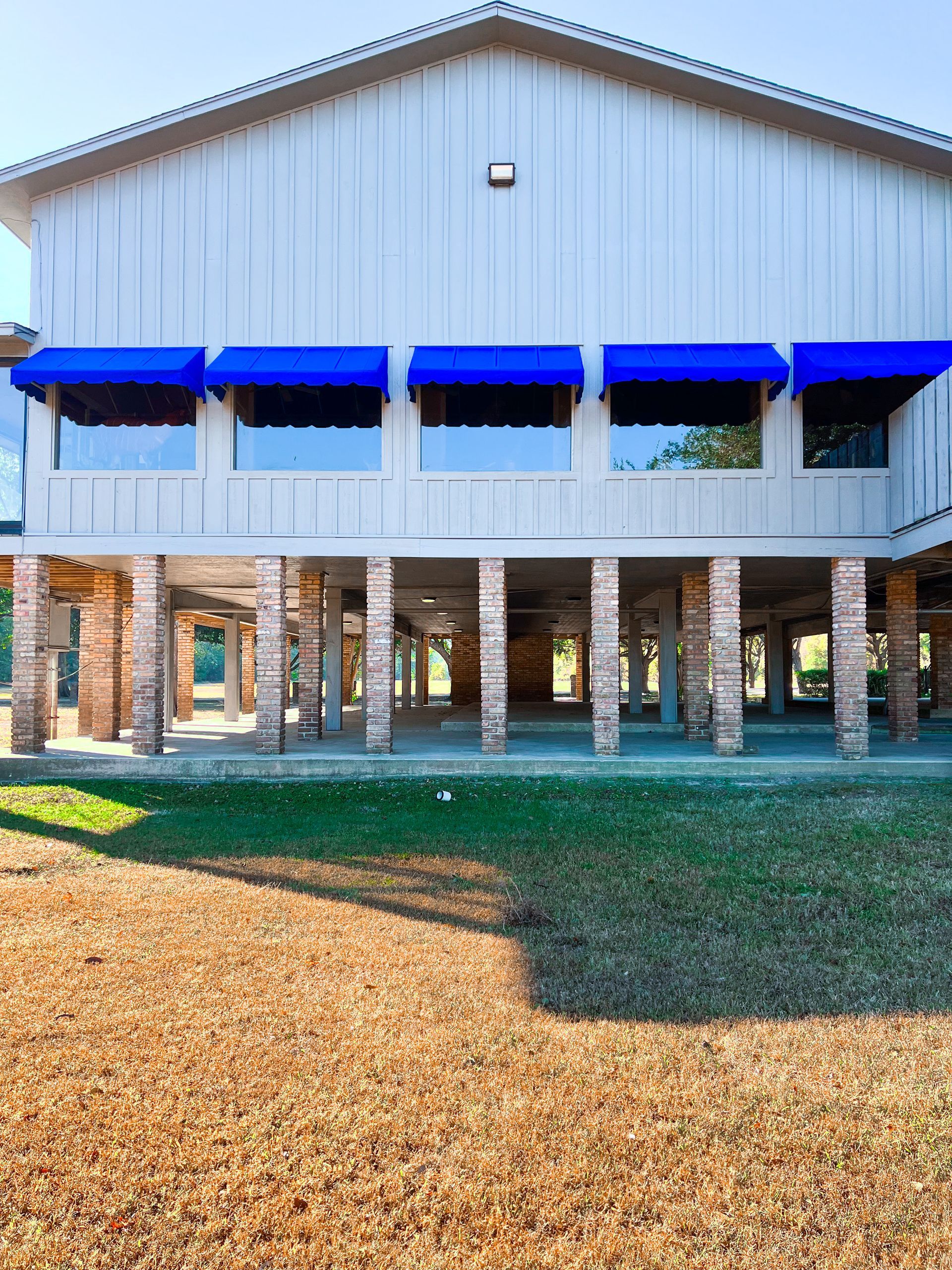 Building with blue awnings on brick pillars; green lawn, sunny.
