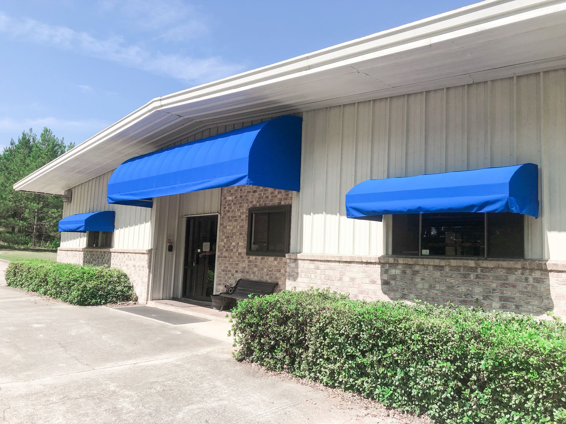 Building with blue awnings over windows and entrance, set against a cloudy sky.