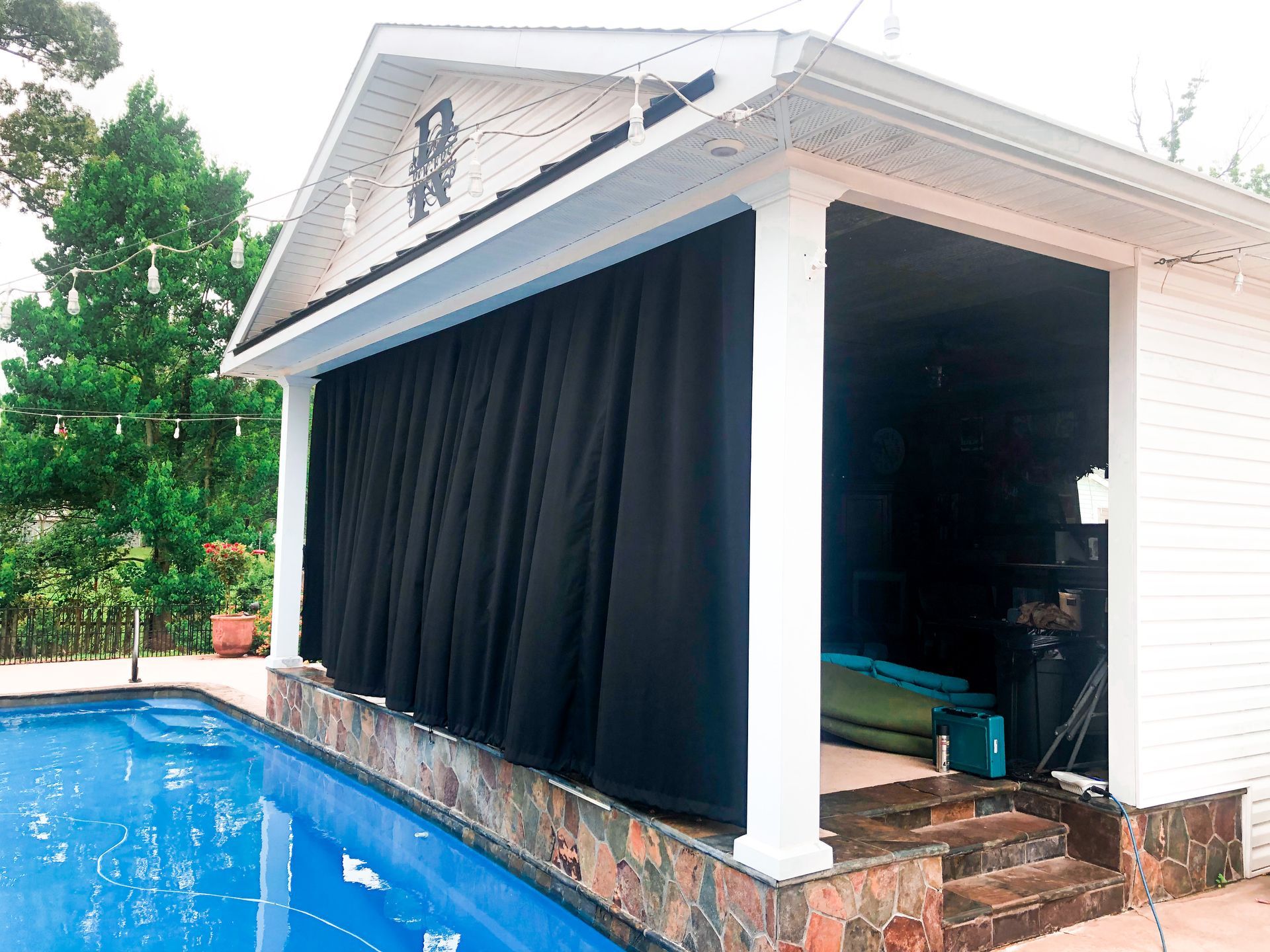 Poolside cabana with black curtains, blue pool, and white columns.