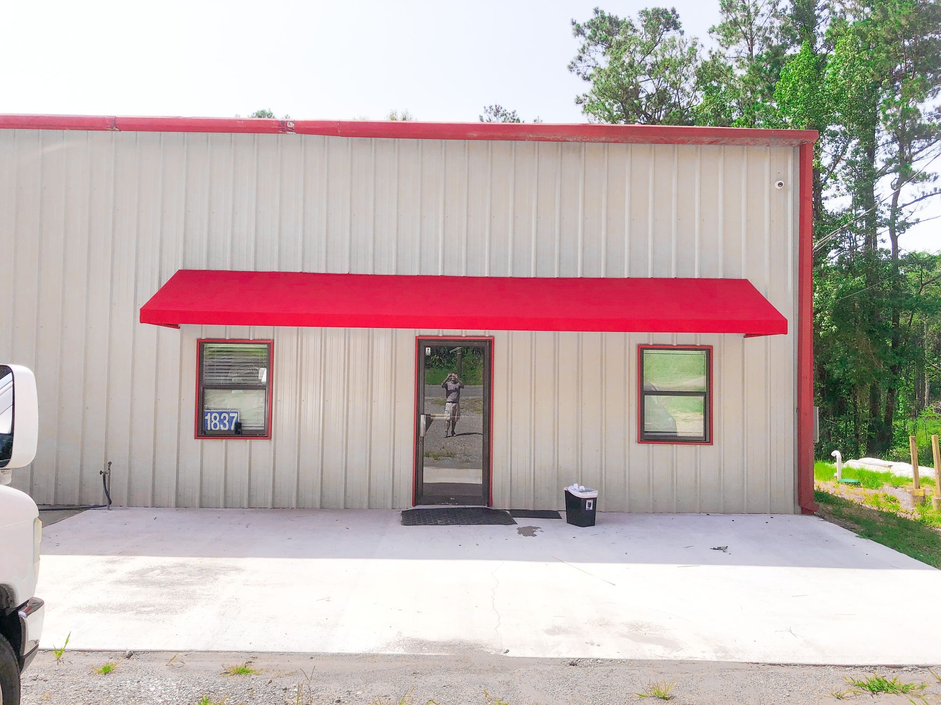 Red awning over a building entrance, flanked by windows. Gray metal siding and red roof.