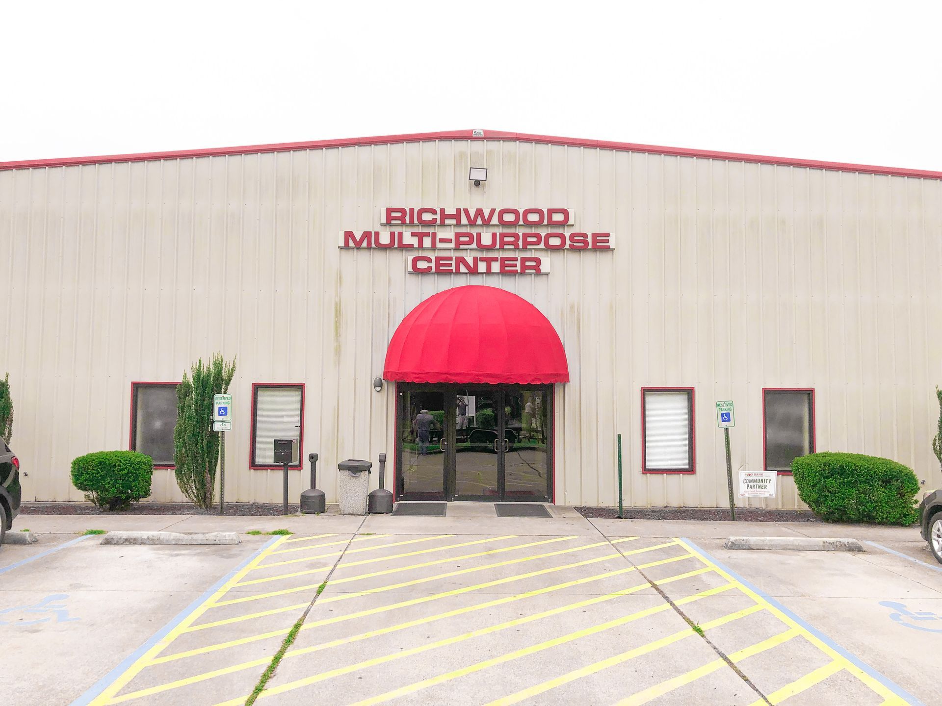 Richwood Multi-Purpose Center exterior, tan building with red awning over entrance, accessible parking sign visible.