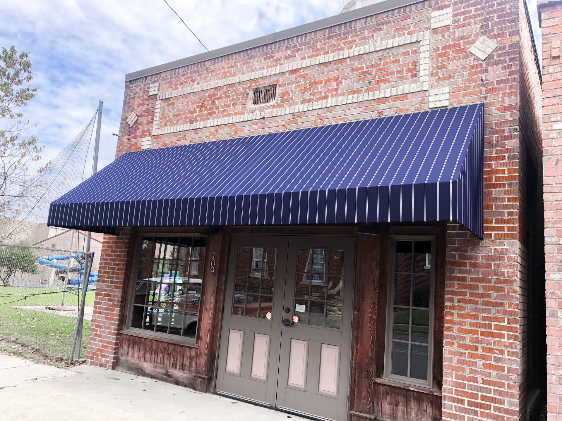 Brick building with blue and white striped awning over a wooden door and windows.
