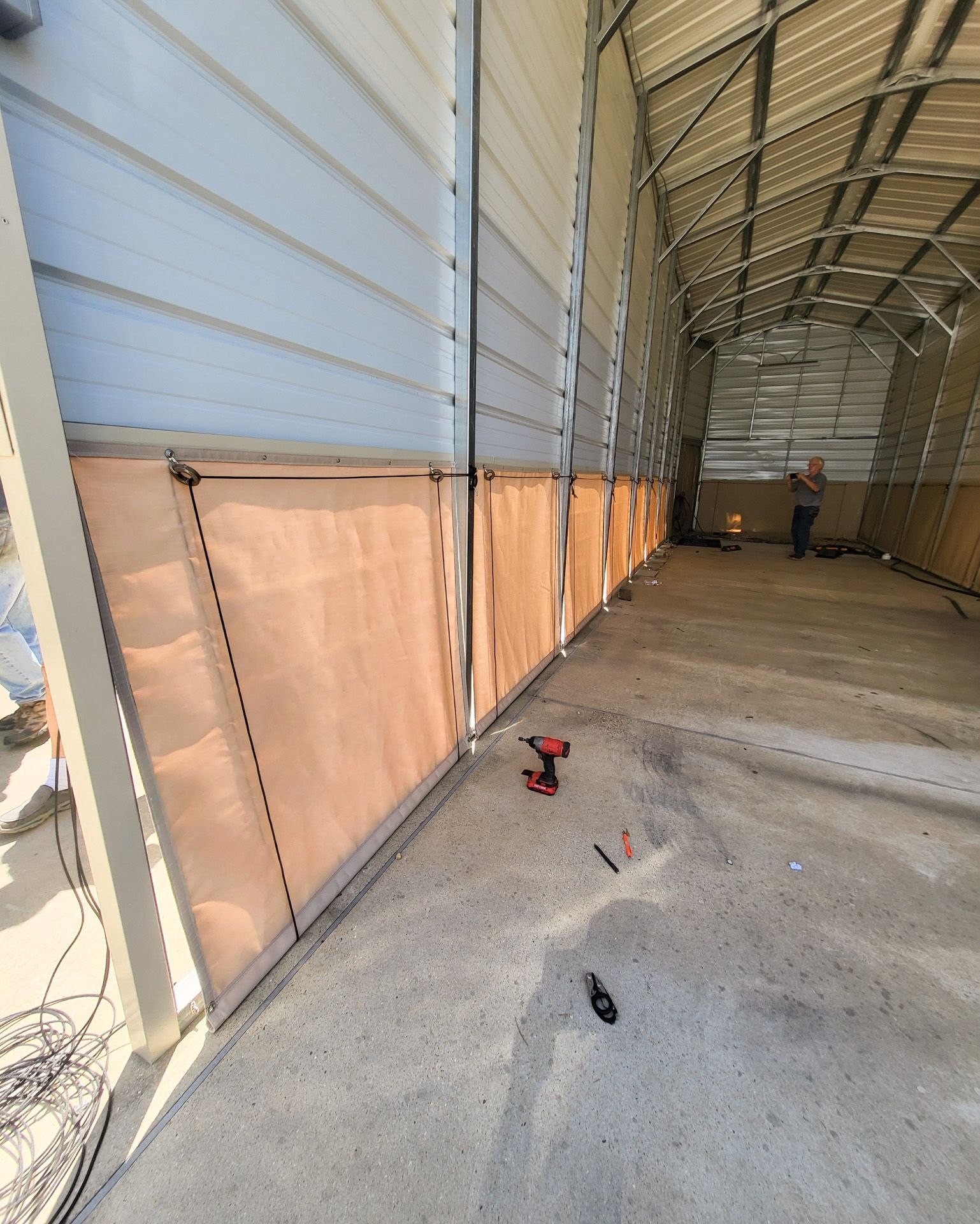 Inside a metal building: insulation panels attached to the wall; worker in the background.
