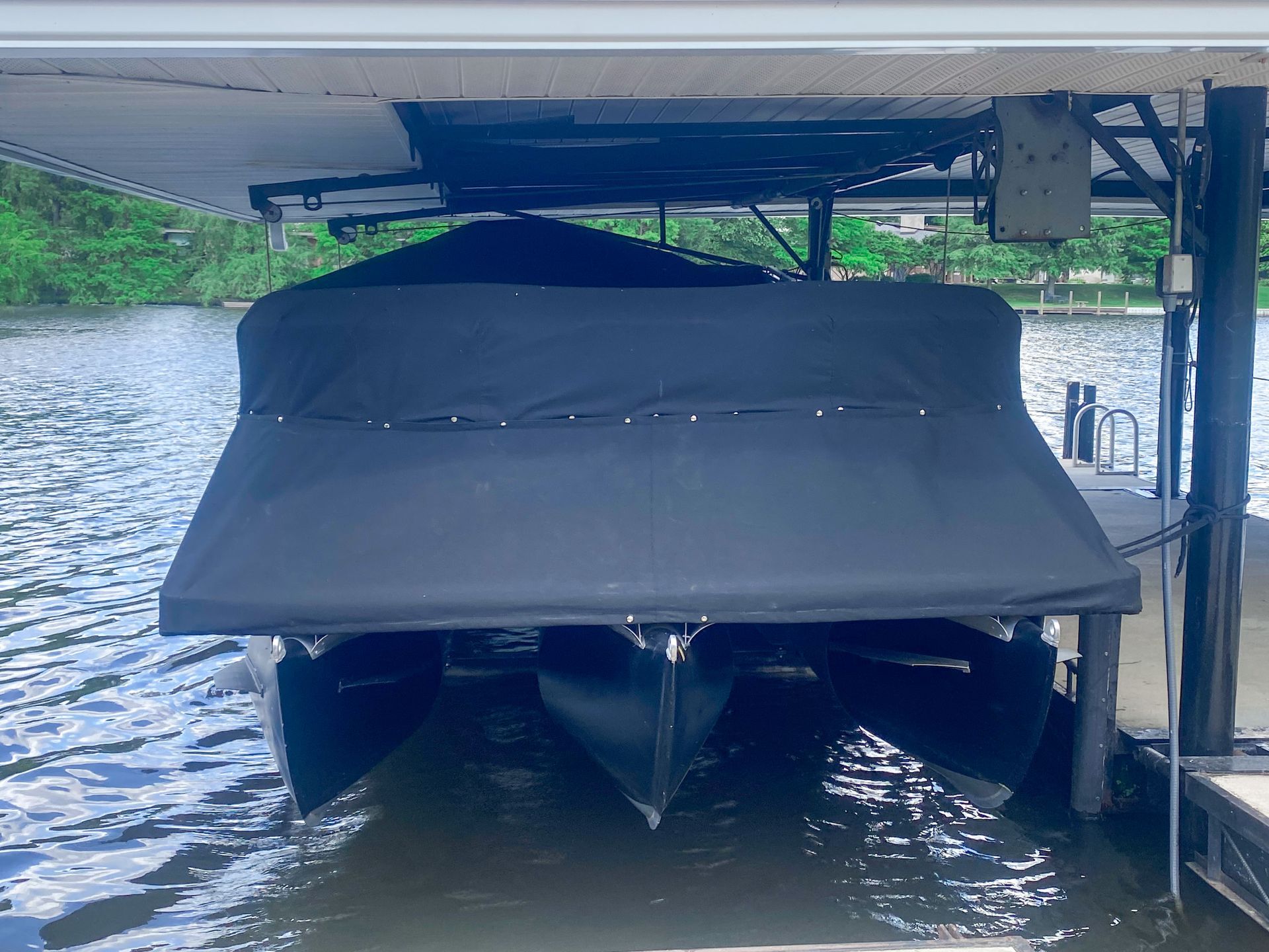 Pontoon boat under a black canopy on a lift, in a boat slip.
