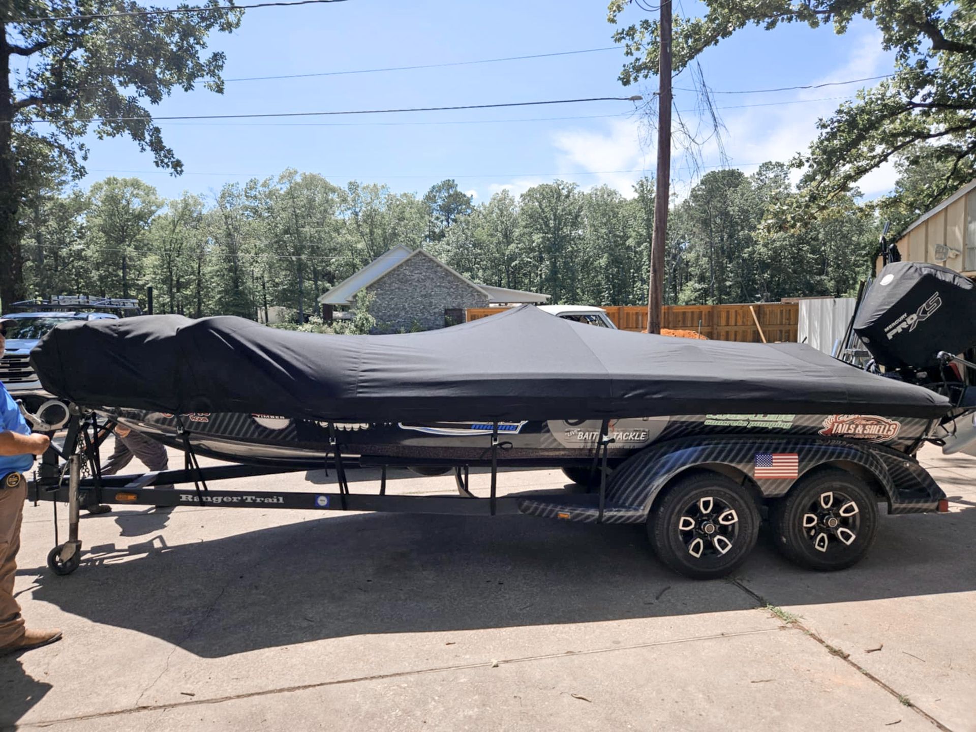 Black boat cover on a trailer outdoors. Boat is on a black trailer with dual axles, American flag sticker.