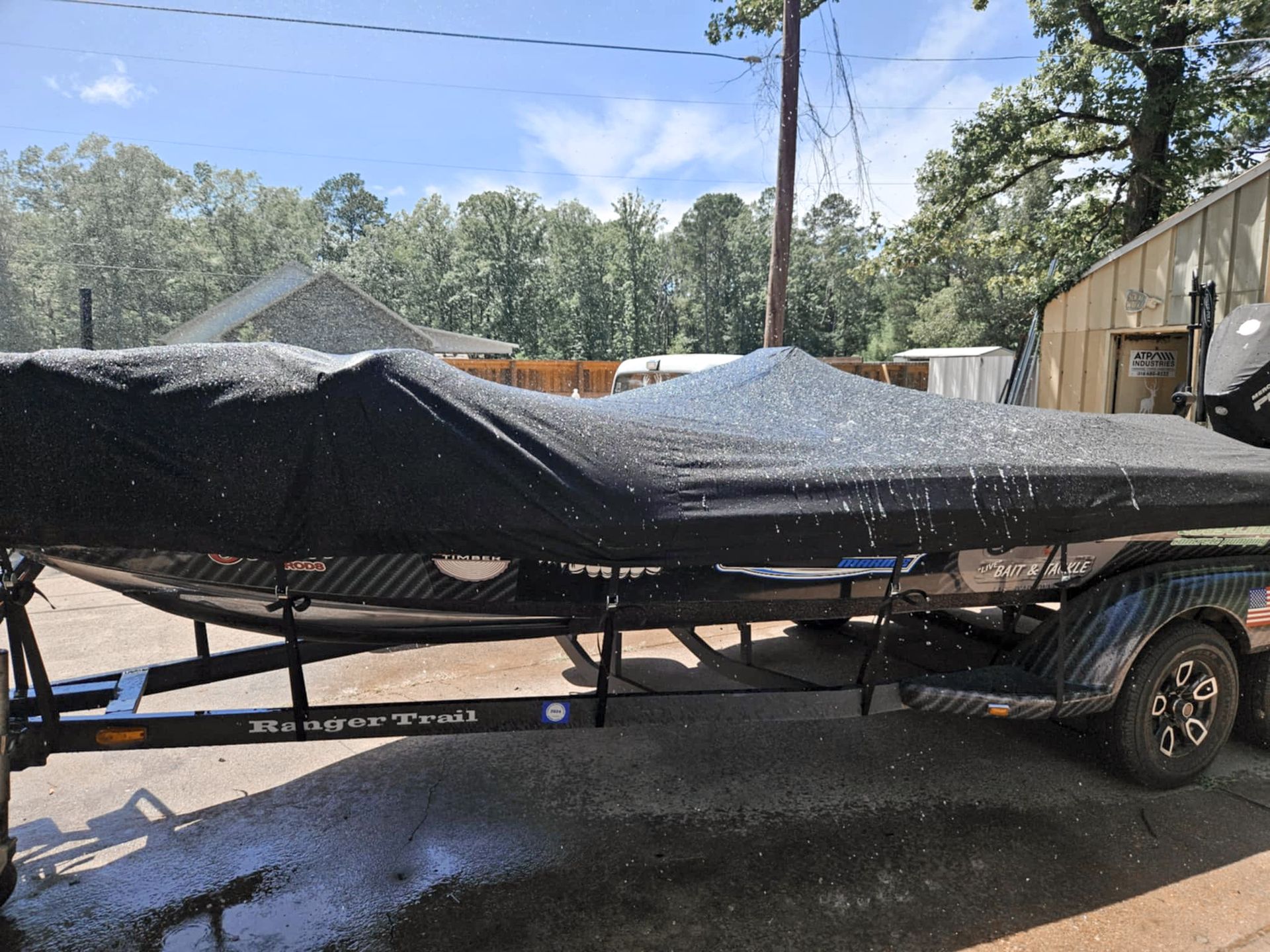 Boat on trailer, covered in black, with soapy water droplets. Outdoors, sunny day.