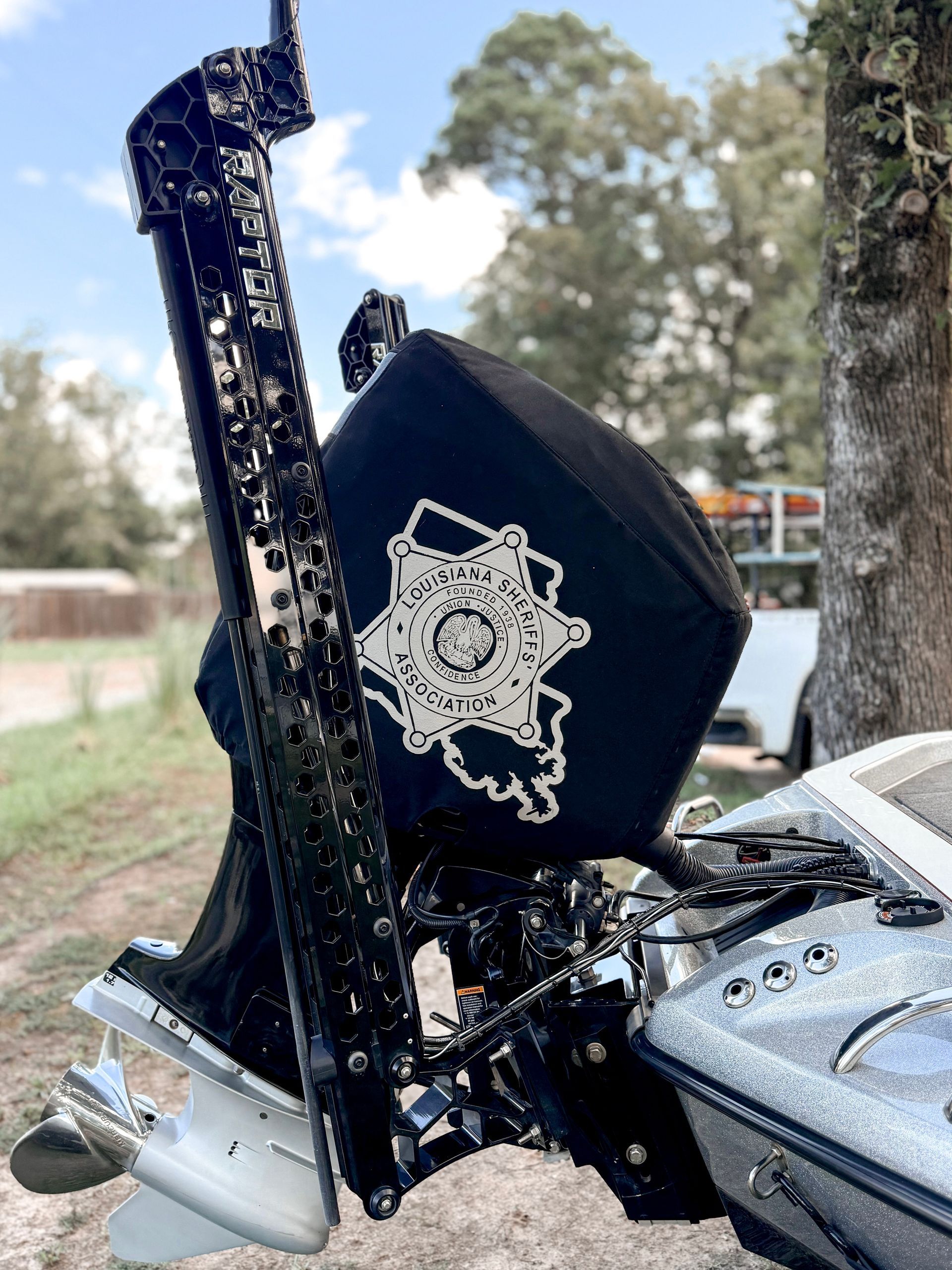 Boat motor with a black cover and a white emblem, on a boat near trees.