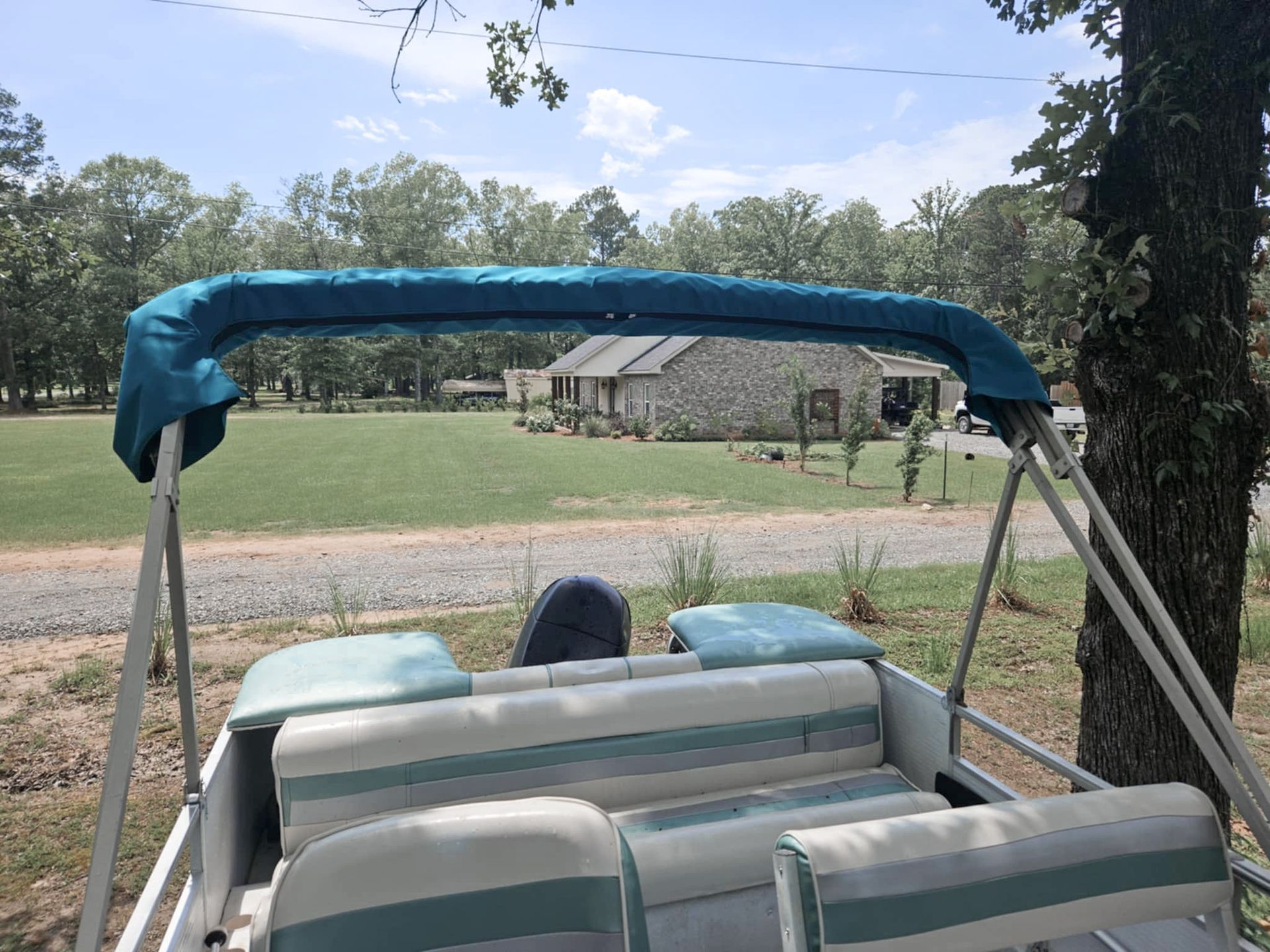 Pontoon boat with teal canopy and seats, on grass with trees and a house in the background.