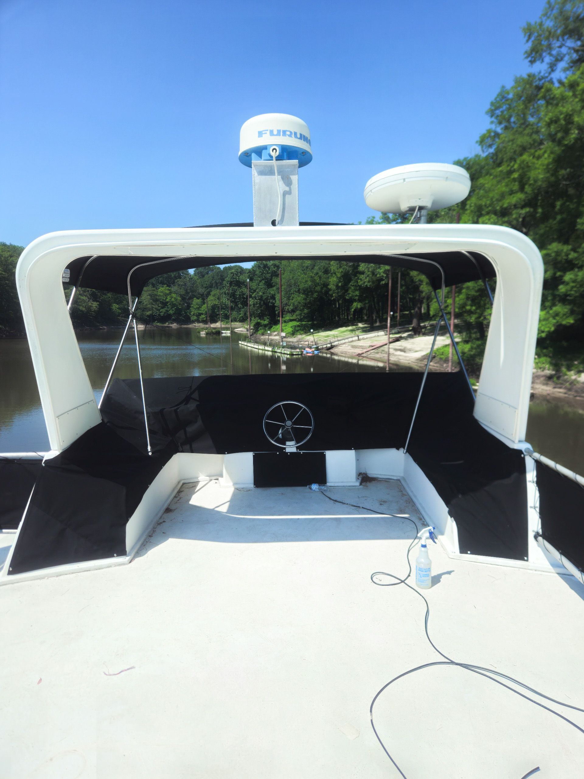 Rear view of a white boat on a river, with radar dome and black shaded cockpit.