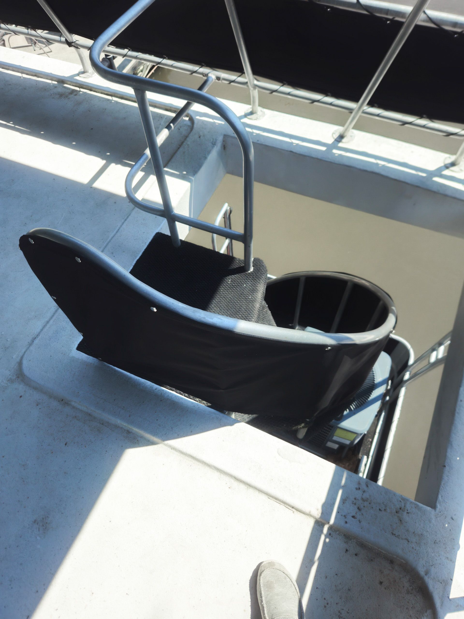 Black chair-like lift to assist someone in getting into the interior of a boat. Metal rails provide assistance.