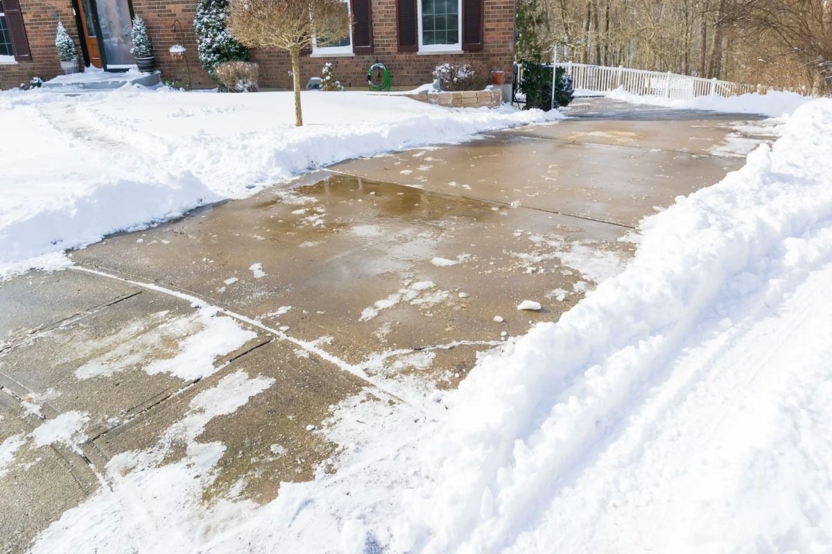 Snow-cleared concrete driveway bordered by high snowbanks beside a brick house