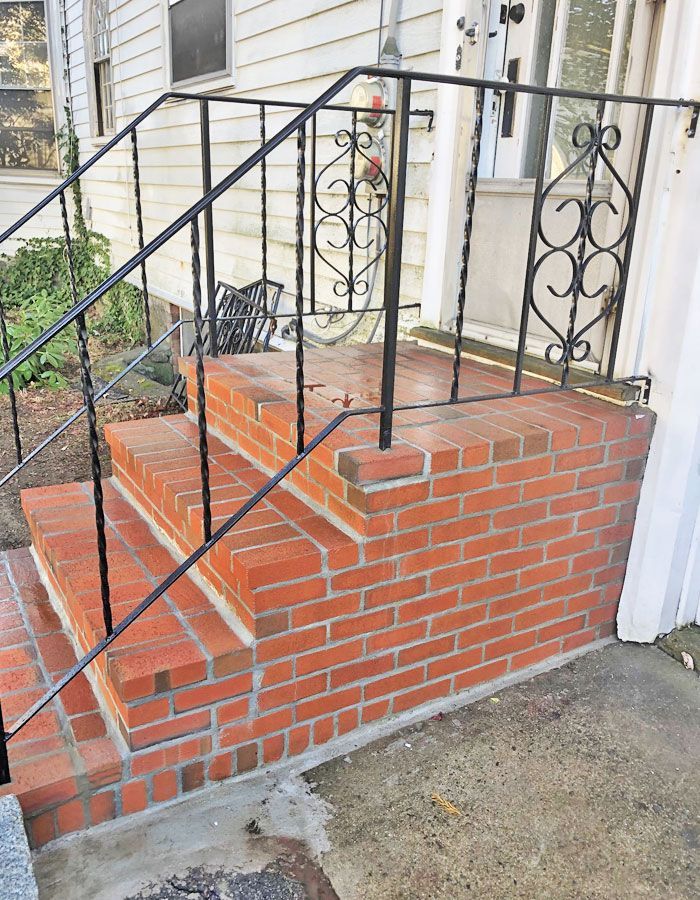 Brick front steps with black wrought-iron railings leading to a porch entrance