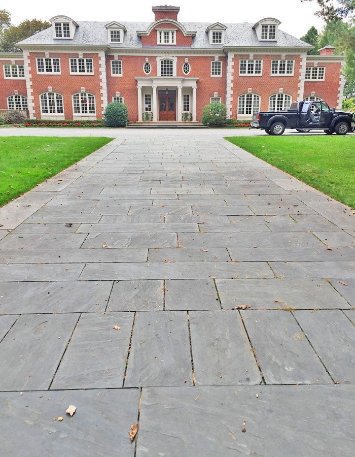 Stone walkway leading to a red-brick mansion with a parked black SUV on the right.