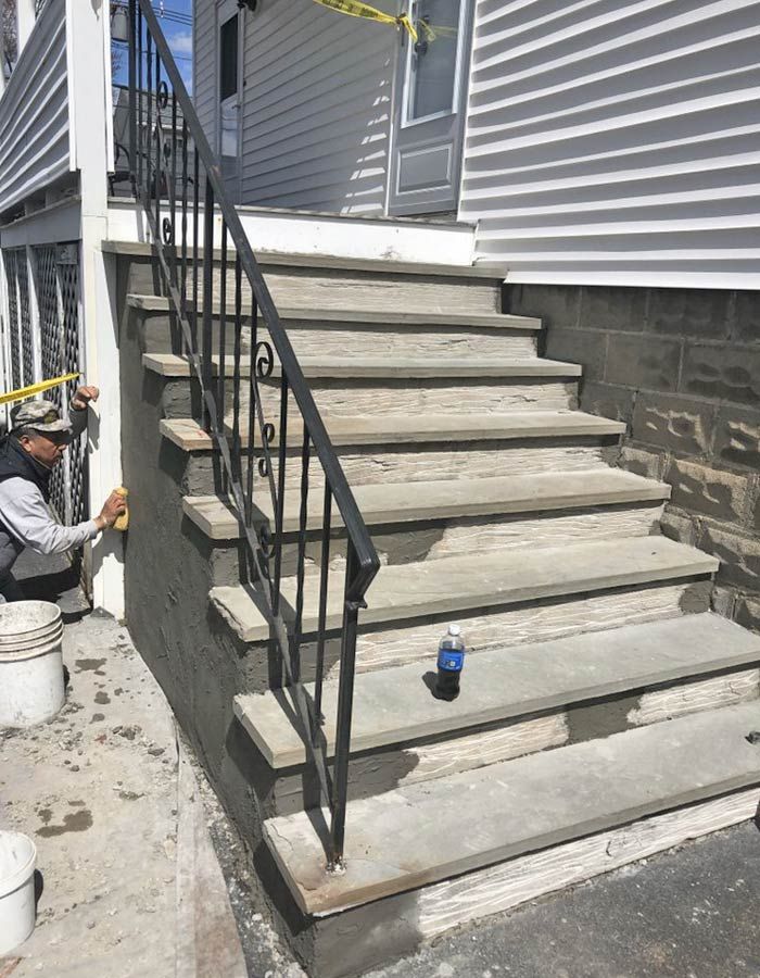 Concrete outdoor stairs with black metal railings beside a house; worker crouches at left during construction.