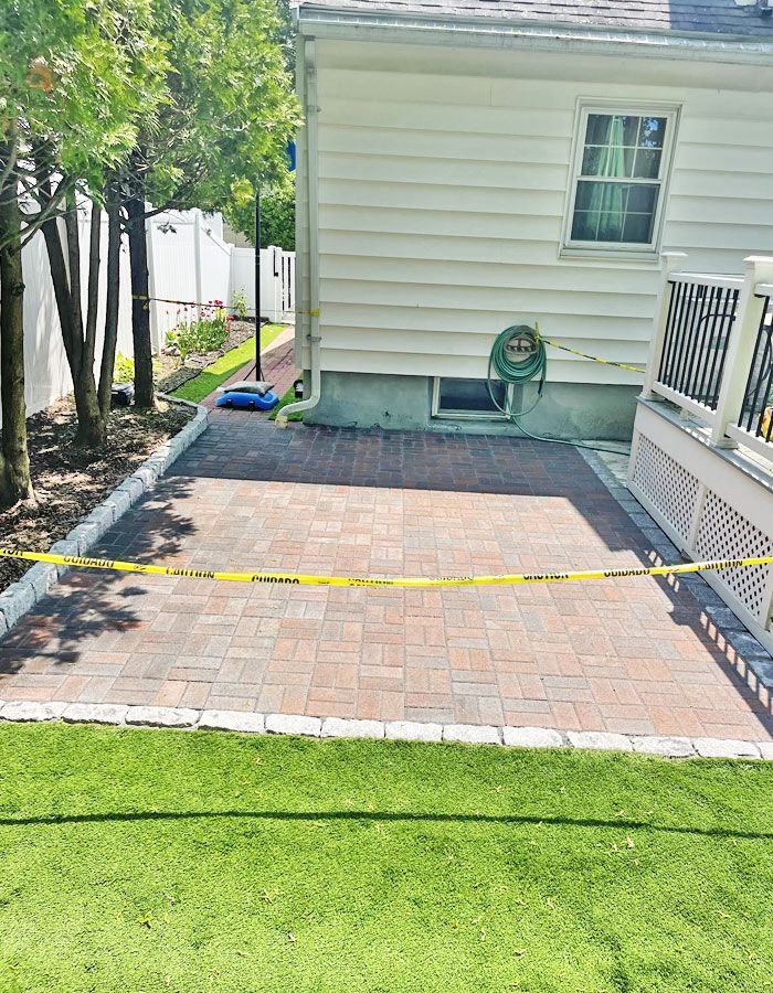 Brick patio beside a house, cordoned off with yellow caution tape and bordered by grass and a railing.