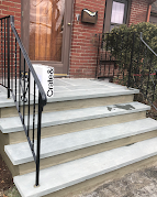 Brick house front steps with white concrete stairs, black railing, and wooden front door