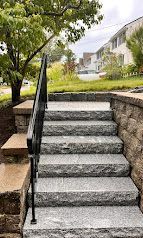 Stone steps with black railing leading up to a landscaped apartment building entrance