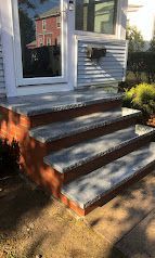 Front steps with white trim and red brick facing, leading to a house entrance in sunlight