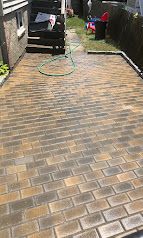 Long brick driveway with a garden hose, van at the far end, and laundry hanging near a fence