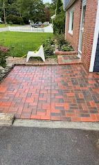 Brick patio beside a brick house with a white chair, planter, and lawn beyond the driveway