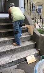 Person climbing outdoor concrete steps beside a house, with a wooden ramp and handrails nearby