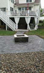 Backyard paver patio with a square fire pit in front of a raised deck and stairs