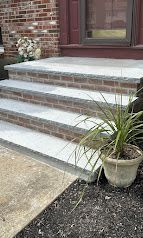 Front steps with white tile treads beside a brick house, with a potted plant in the foreground