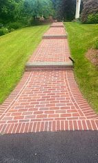 Brick walkway with low steps, bordered by green grass and trees.