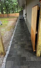 Narrow dark-tiled walkway beside a house, with a wooden fence and outdoor furniture in the distance.