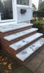 Brick front steps with white treads dusted in snow, leading to a house entrance and mailbox.