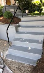 Freshly painted gray outdoor steps with a black handrail leading up to a house entrance