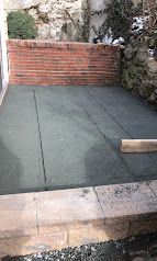Small patio with green flooring, brick wall, and stone edging beside a rocky garden.