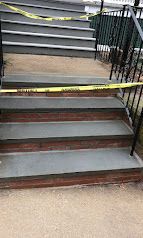 Staircase with a yellow caution tape barrier across the steps and black railings on both sides