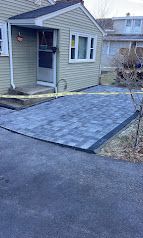 Concrete wheelchair ramp leading to a small house entrance from a paved driveway